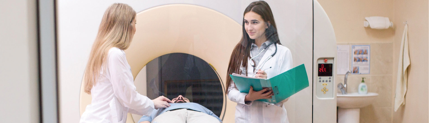 Two hospital personnel standing over patient during PET scan