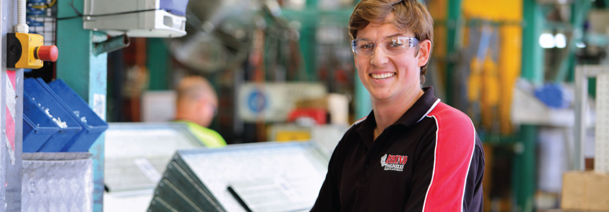 smiling worker in factory standing in front of machine