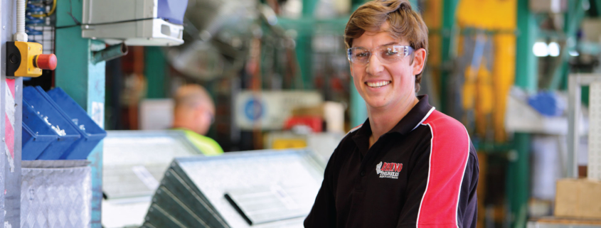 smiling worker in factory standing in front of machine