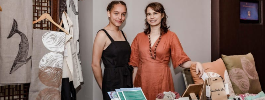 Two smiling Aboriginal and Torres Strait Islander women standing behind a table display