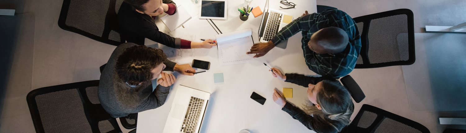 Men and women gathered around a desk looking at paperwork between them