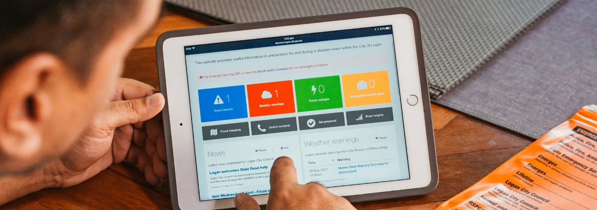 Man using tablet computer, with Logan Disaster Dashboard on the screen