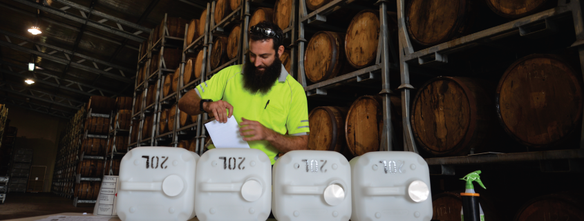 Man putting labels on sanitiser bottles in rum barrel warehouse