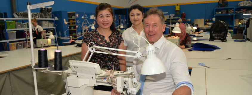 City of Logan Mayor Darren Power gets some sewing tips from machinists Charlene Kim (left), of Kuraby, and Annabella Lewis, of Marsden.