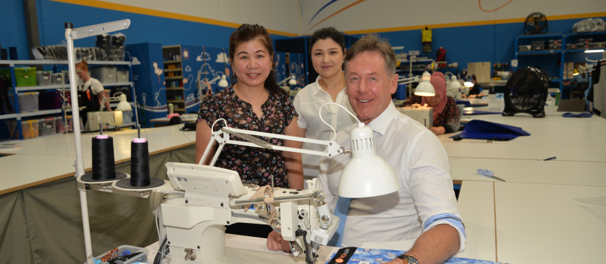 City of Logan Mayor Darren Power gets some sewing tips from machinists Charlene Kim (left), of Kuraby, and Annabella Lewis, of Marsden.