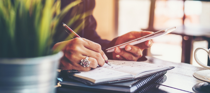 A lady looking at her phone and writing on a notebook