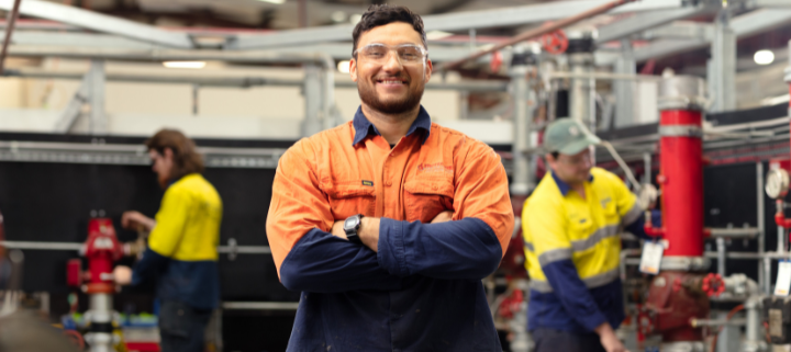 A tradesman standing in front of the machines crossing his arms and smiling at the camera