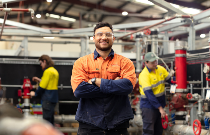 A tradesman standing in front of the machines crossing his arms and smiling at the camera