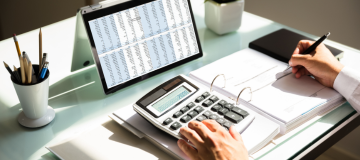 A tablet with numbers on a spreadsheet, a person taking notes while using a calculator