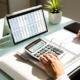 A tablet with numbers on a spreadsheet, a person taking notes while using a calculator