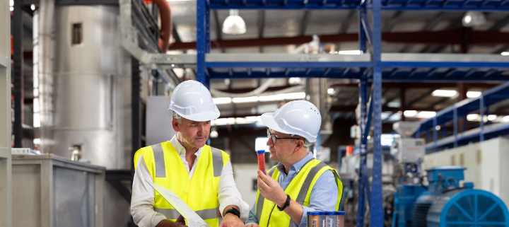 2 men wearing high-vis vests and hard hats standing and talking in the manufacturer.