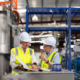 2 men wearing high-vis vests and hard hats standing and talking in the manufacturer.