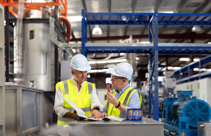 2 men wearing high-vis vests and hard hats standing and talking in the manufacturer.