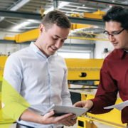 2 people in the manufacturing warehouse pointing at a tablet and discussing