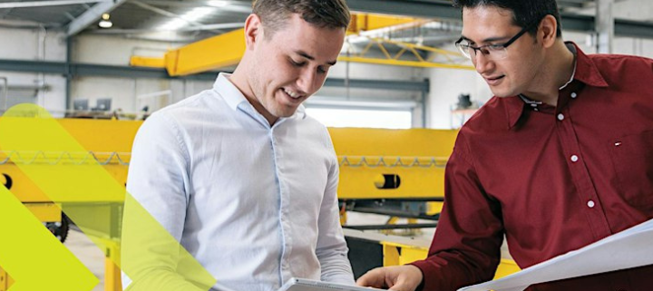 2 people in the manufacturing warehouse pointing at a tablet and discussing