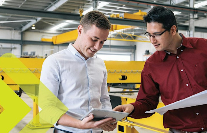 2 people in the manufacturing warehouse pointing at a tablet and discussing