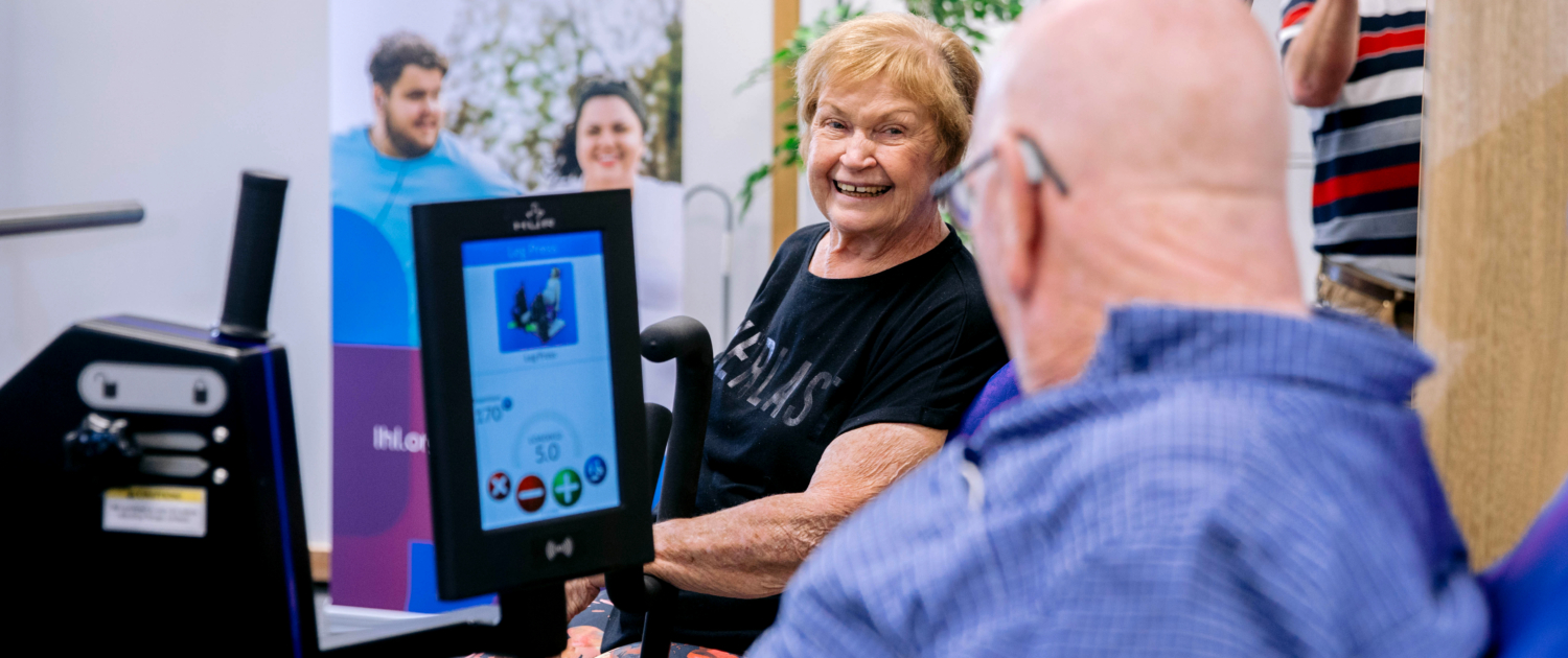 2 elders having a chat while sitting on a gym machine.