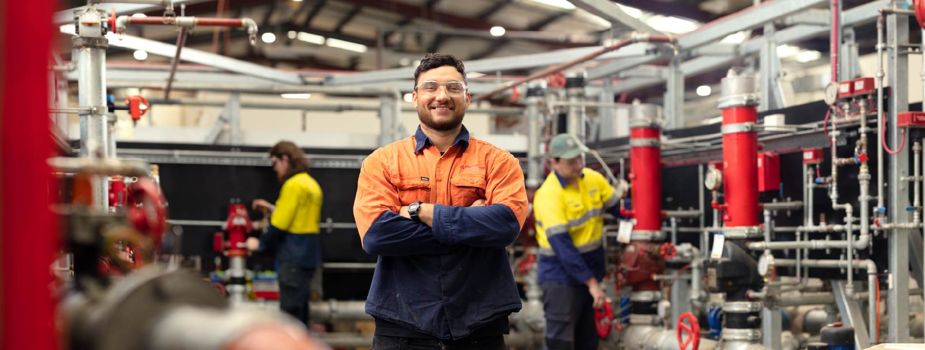 A tradesman standing in front of the machines crossing his arms and smiling at the camera